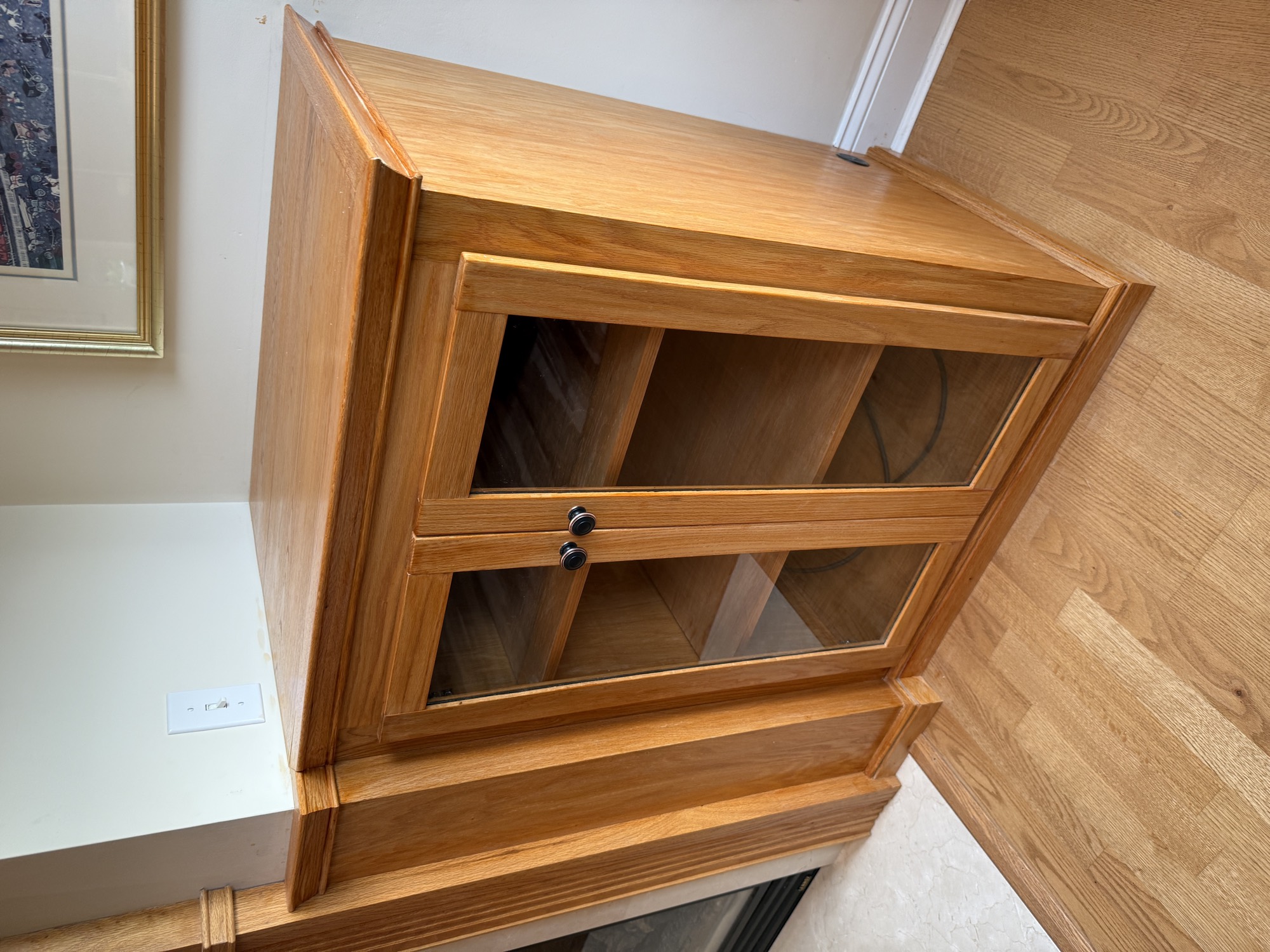 Detail of a finished oak built-in cabinet with glass doors and adjustable shelves beside the fireplace